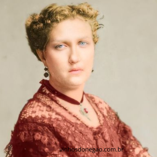 Retrato colorido digitalmente da Princesa Isabel do Brasil, vestindo traje de renda bordô, com detalhes em veludo no pescoço e joias da época, Ela possui cabelos loiros cacheados e olhos azuis, olhando fixamente para a câmera. Ela era lindímiima.
